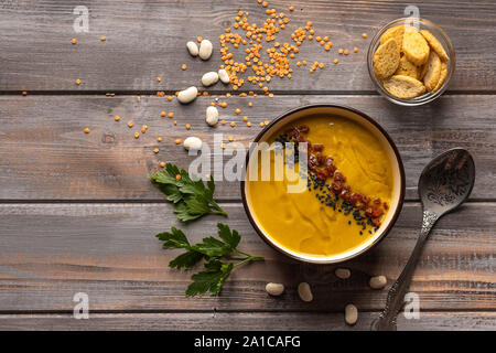 Minestra di crema con una miscela di fagioli e spezie su uno sfondo di legno. accanto a un cucchiaio e una ciotola di cracker Foto Stock