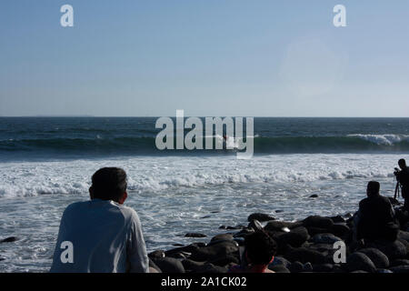 Spettatori uomo, donna, fotografo visualizzando la maestria di un surfista che emozioni sopra le onde nel mare della Baja California Messico Foto Stock