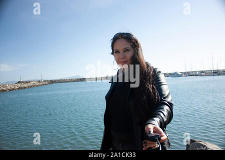 Rocky donna che indossa un nero giacca di pelle e occhiali da sole con una giacca di pelle guardando l'orizzonte nel mare della Baja California Messico mentre doin Foto Stock