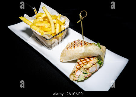 Una gustosa di gamberi e avocado servito in una tortilla avvolgere con salsa di frutti di mare e accompagnato con un lato di patatine fritte Foto Stock