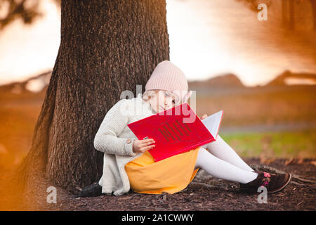 Piccola ragazza caucasica è la lettura del libro sotto la caduta tree Foto Stock