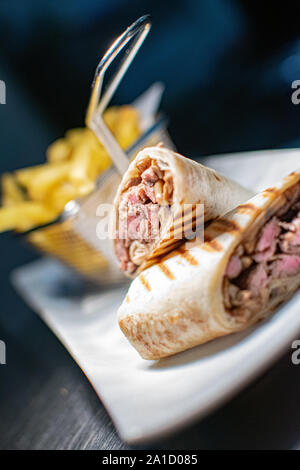 Un'immagine ravvicinata di un filetto alla griglia steak Tortilla avvolgere cucinato alla perfezione e serviti con una porzione di patate fritte Foto Stock