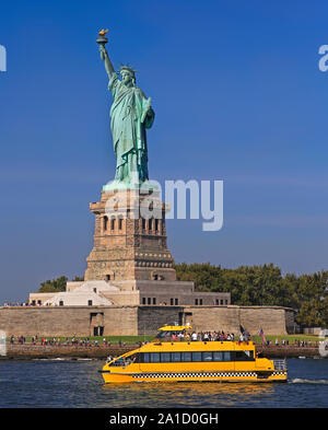 La statua della Libertà con acqua di colore giallo taxi boat in primo piano, New York City, Stati Uniti d'America Foto Stock