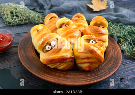 Divertente e salsiccia cotolette mummie in pasta con gli occhi, ketchup sul tavolo. Cibo di Halloween. Foto Stock