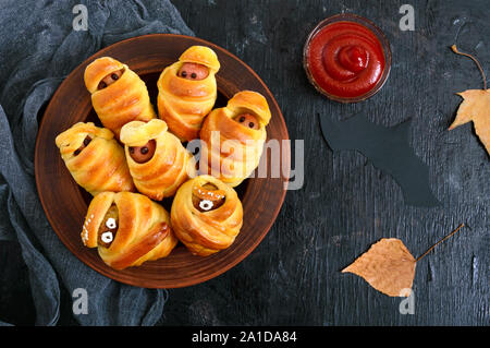 Divertente e salsiccia cotolette mummie in pasta con gli occhi, ketchup sul tavolo. Cibo di Halloween. Vista dall'alto. Lay piatto Foto Stock