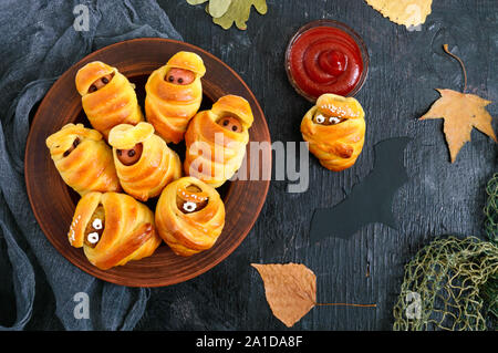 Divertente e salsiccia cotolette mummie in pasta con gli occhi, ketchup sul tavolo. Cibo di Halloween. Vista dall'alto. Lay piatto Foto Stock