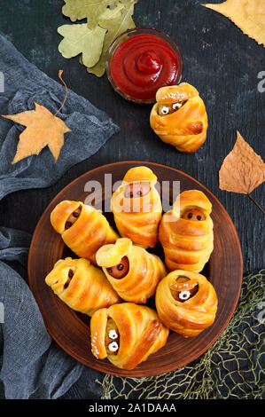 Divertente e salsiccia cotolette mummie in pasta con gli occhi, ketchup sul tavolo. Cibo di Halloween. Vista dall'alto. Lay piatto Foto Stock