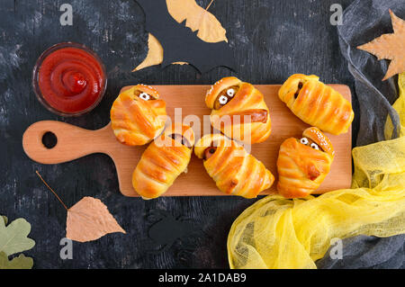 Divertente e salsiccia cotolette mummie in pasta con gli occhi, ketchup sul tavolo. Cibo di Halloween. Vista dall'alto. Lay piatto Foto Stock