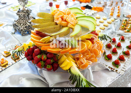 Colorata frutta fresca sul tavolo bianco. Pere, tangerini, fragole, arance, ananas melone frutta estiva Foto Stock