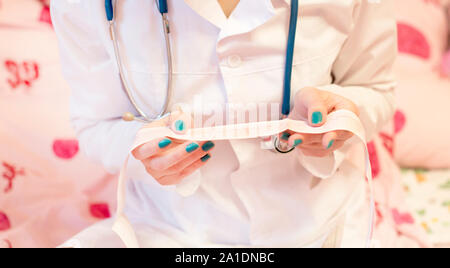 Un medico con uno stetoscopio e mantello bianco controlla un paziente il cardiogram Foto Stock