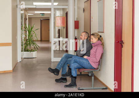 Due persone in una sala di attesa, corridoio con l uomo e la donna seduta su una sedia Foto Stock