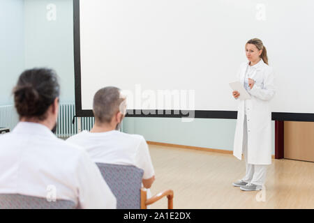 Medico donna è in piedi di fronte a una lavagna vuota dando una lezione o briefing per il personale medico Foto Stock