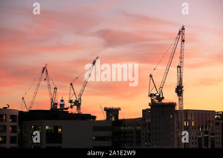 Gru su edifici essendo costruito a Kings Cross, al tramonto, nel nord di Londra, Inghilterra, Regno Unito Foto Stock