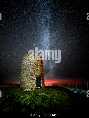 La Via Lattea su Twr Foel Fawr in Mynytho, un mulino a vento abbandonato sul Lleyn Peninsula Galles del Nord come l'ultima luce crea una drammatica bagliore rosso. Foto Stock