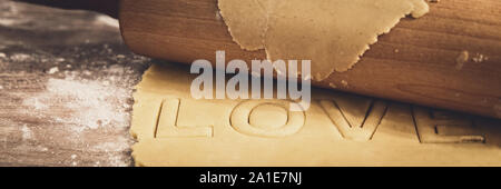 Panorama, luminoso fresco pasta biscotto e perno di rotolamento, la parola amore sono intaglio Foto Stock