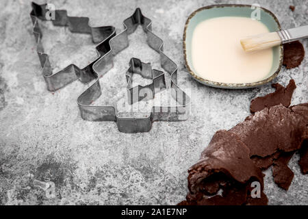 Il cioccolato pasta biscotto, albero di natale taglierine, latte e pasticceria pennello su sfondo grigio Foto Stock