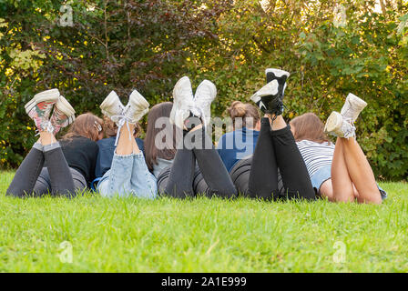 Vista delle gambe e scarpe di una gang di giovani ragazze adolescenti in piedi sull'erba di un parco. Avendo divertimento all'aperto in estate. Godersi la vacanza Foto Stock