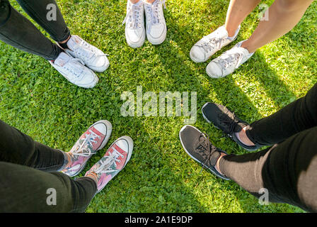 Vista dall'alto di scarpe di una gang di giovani ragazze adolescenti in piedi in cerchio sul prato di un parco. Avendo divertimento all'aperto in estate. Vacanze Foto Stock