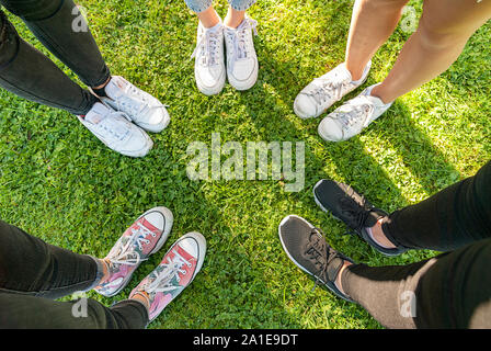 Vista dall'alto di scarpe di una gang di giovani ragazze adolescenti in piedi in cerchio sul prato di un parco. Avendo divertimento all'aperto in estate. Vacanze Foto Stock