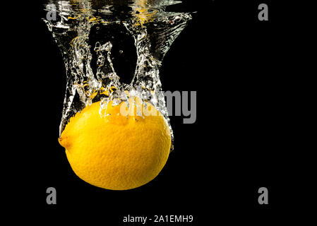 Fresche limone giallo in acqua splash su sfondo nero con un sacco di bolle di aria. Foto Stock