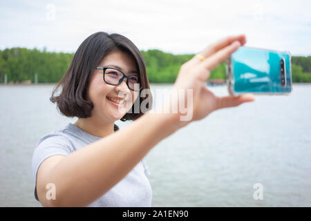 Bella giovane donna tenendo un smartphone. Per scattare una foto di te stesso da un telefono con fotocamera (Selfie). Il concetto di turismo da soli Self-portrait p Foto Stock