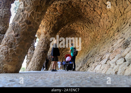 La gente a piedi attraverso il colonnato di organico colonne di pietra nel Parco Guell, progettato da Antonio Gaudí Barcelona, Spagna Foto Stock