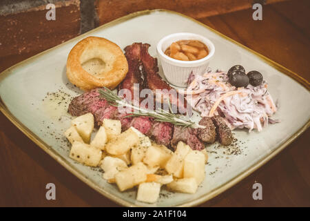 In estate la cena arrosto di erba Australiano-fed bistecca di fianco (150 gm), carni bovine pancetta, fagioli al forno, coleslaw, rosso insalata di patate, Yorkshire pudding, peppercor nero Foto Stock