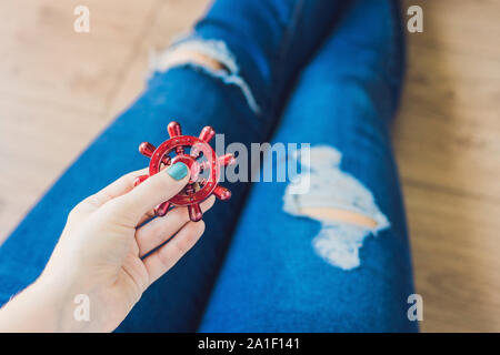 Ragazza adolescente in holey jeans tiene in mano e gioca con un dispositivo a rotazione vorticosa. Foto Stock