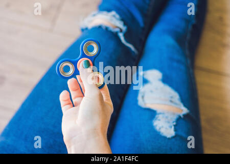 Ragazza adolescente in holey jeans tiene in mano e gioca con un dispositivo a rotazione vorticosa. Foto Stock