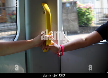 Sole illumina le mani di un ragazzo e una ragazza in possesso di una maniglia su un tram in movimento, sfondo sfocato, comportamento sicuro nel traffico e vicino fino Foto Stock