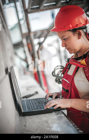 Femmina ingegnere architetto sta alta sul ponteggio ispeziona e controllare i progressi compiuti a livello sito in costruzione sul computer portatile Foto Stock