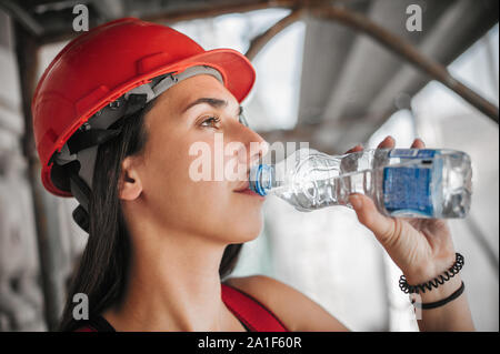 Costruzione femmina mason lavoratore seduto ad alta sul ponteggio, riposo e acqua potabile Foto Stock