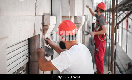 Due lavoratori sta alta sul ponteggio, stuccatura e rinnovando la parete sul vecchio edificio di utilità Foto Stock