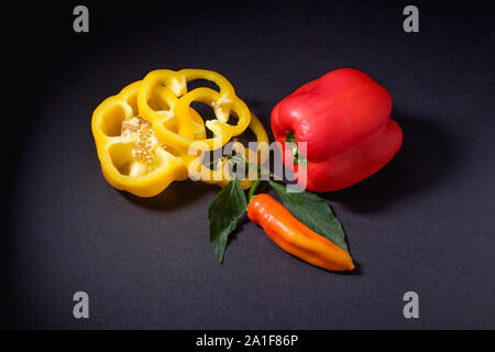 Fette di peperone giallo con tutto il peperone rosso e un rosso pepe banana su sfondo scuro Foto Stock