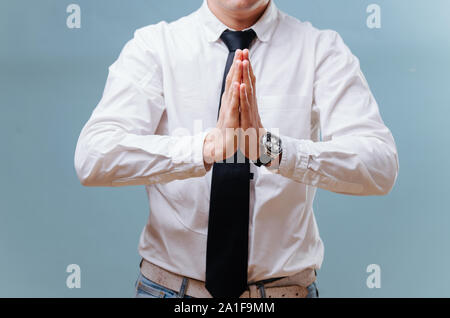 Imprenditore in maglia bianca unendo le sue mani, rendendo il gesto di preghiera su blu Foto Stock