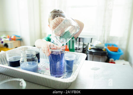 Anonimo bambino versa il liquido blu in vetro durante la scienza esperimento Foto Stock