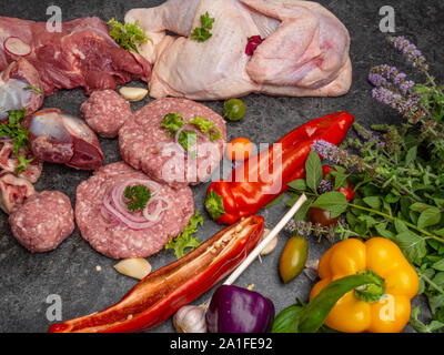 I diversi tipi di carne cruda: manzo, pollo, agnello, Gilbert, maiale, erbe aromatiche, lattuga, aglio, pomodori ciliegini, il peperone verde, vicino fino Foto Stock