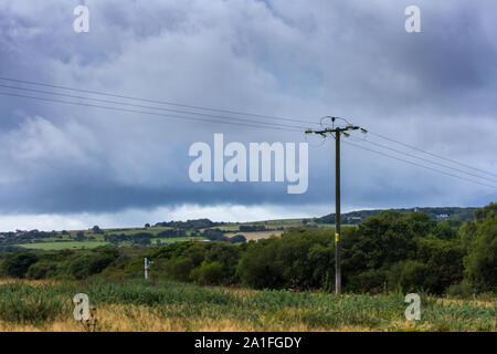 Le linee di alimentazione attraversando la campagna con pioggia nuvole temporalesche, Dorset, Regno Unito Foto Stock