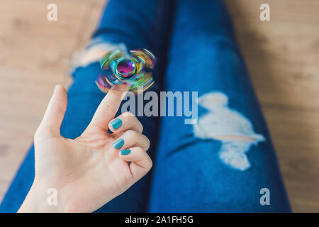 Ragazza adolescente in holey jeans tiene in mano e gioca con un dispositivo a rotazione vorticosa. Foto Stock