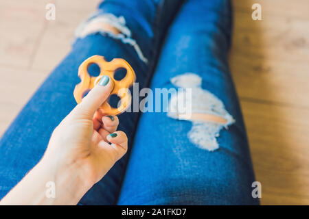 Ragazza adolescente in holey jeans tiene in mano e gioca con un dispositivo a rotazione vorticosa. Foto Stock