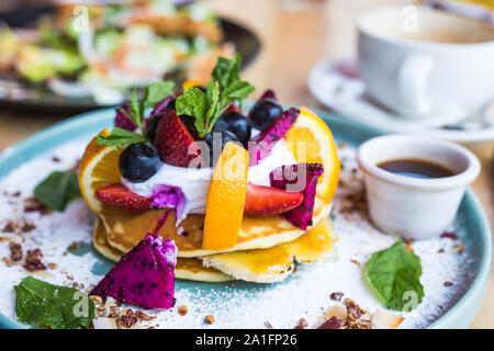Una pila di pancake con frutta varia, dragon di frutta e mirtilli e sciroppo Foto Stock