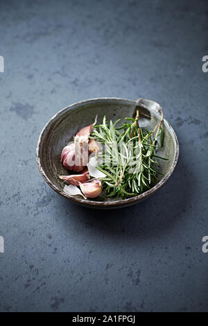 Di rosmarino fresco e aglio in un recipiente di ceramica Foto Stock