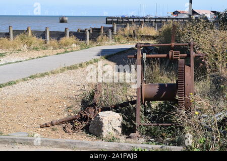 Il vecchio metallo arrugginito verricello in barca sulla spiaggia con il porto e il mare per centrali eoliche in distanza in estuario del Tamigi Foto Stock