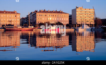 Costruzioni mare e piccole imbarcazioni di essere illuminati dal sole al tramonto, sulla città costiera di Rijeka, Croazia Foto Stock