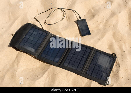 Portatile pannello solare è sulla spiaggia in sabbia e ricarica la batteria del telefono cellulare. Foto Stock