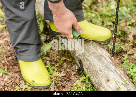 Tourist prepara la legna nel bosco per il campeggio e di sezionatura tramite portable pocket chainsaw Foto Stock