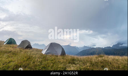 Panorama delle montagne, in una radura, ci sono tre tende sullo sfondo di un deterioramento della situazione meteo e pioggia nuvole al tramonto Foto Stock