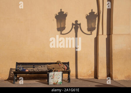 Poveri dorme in corrispondenza del banco vicino al grande porta di legno di el Mansour moschea di Marrakech in Marocco Foto Stock