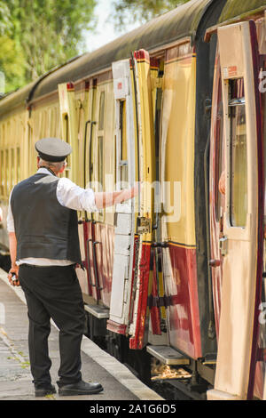 CRANMORE, Inghilterra - Luglio 2019: Protezione in piedi accanto ad un treno in attesa di discostarsi dalla stazione Cranmore sulla East Somerset Railway. Foto Stock