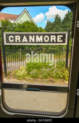 CRANMORE, Inghilterra - Luglio 2019: Stazione segno sulla piattaforma della stazione Cranmore sulla East Somerset Railway visto attraverso la finestra aperta di un treno Foto Stock